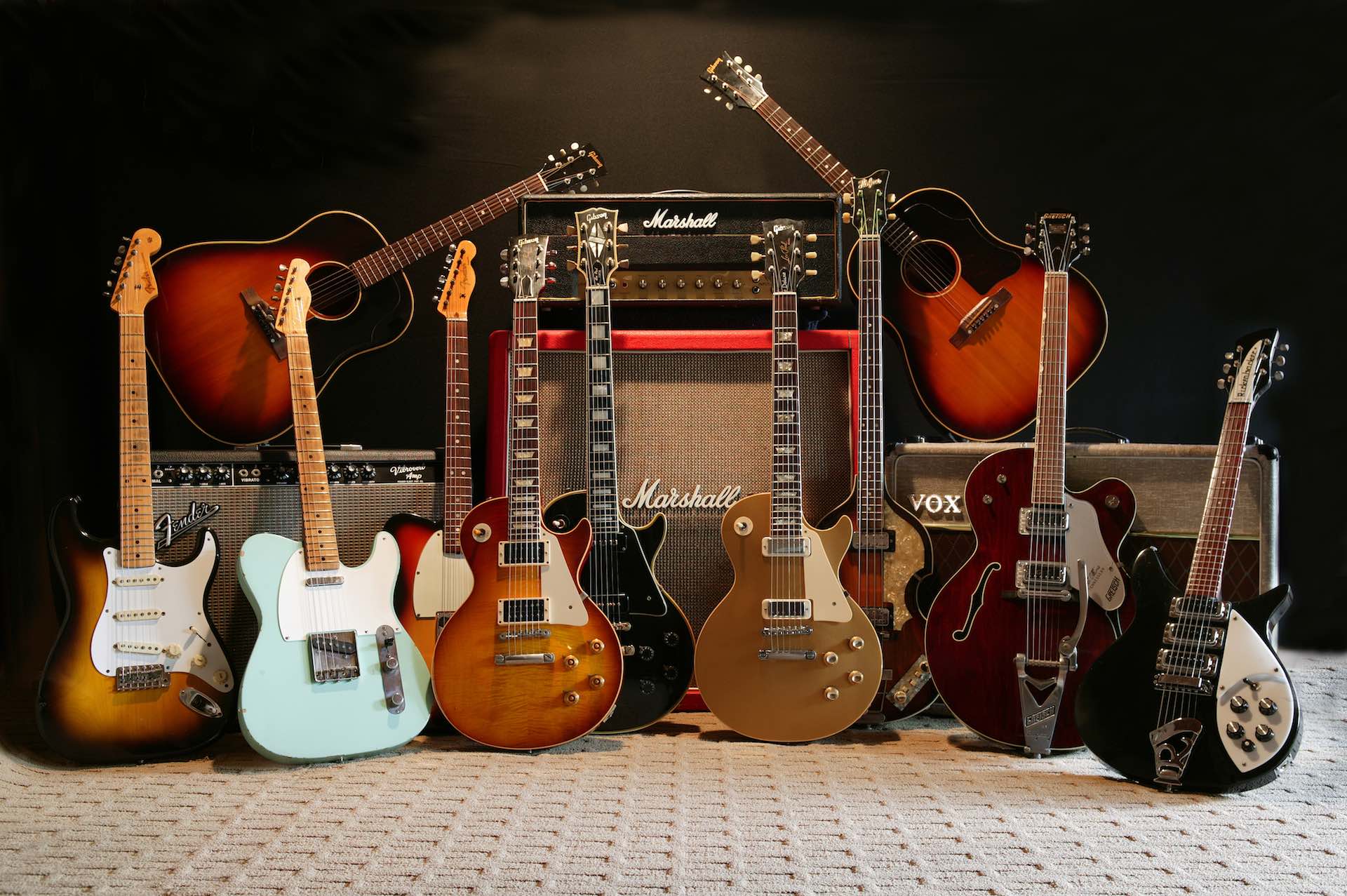 Vintage Fender and Gibson guitars in front of classic Marshall, Fender and Vox amplifiers